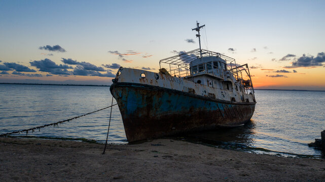 Aerial view of a rusted ship resting on the sandy shore under a dusky sky painted with hues of orange and blue, Ilha de Mocambique, Nampula, Mozambique.