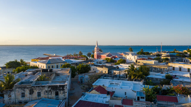 Aerial view of the Island of Mozambique reveals timeworn buildings contrasting with the vibrant pink church against the vast blue ocean, Ilha de Mocambique, Nampula, Mozambique.