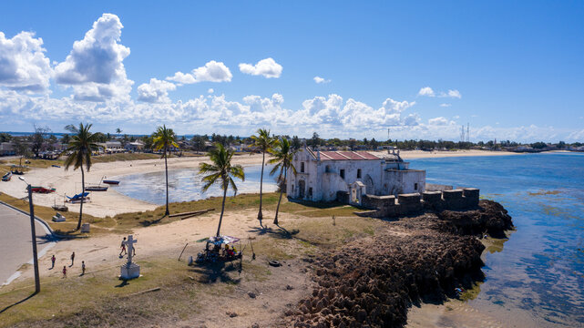 Aerial view of the Chapel of Nossa Senhora de Baluarte standing starkly against the turquoise sea, its white walls contrasting with the dark volcanic rock, Ilha de Mocambique, Nampula, Mozambique.