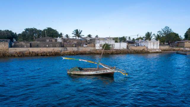 Aerial view of a rustic boat bobs in the cerulean sea against the backdrop of weathered buildings and swaying palms, Ilha de Mocambique, Nampula, Mozambique.