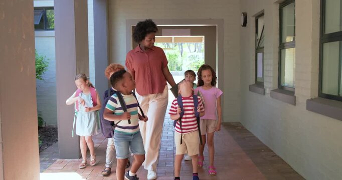 African American woman from doorway leading six children adjusting backpacks while holding tablet