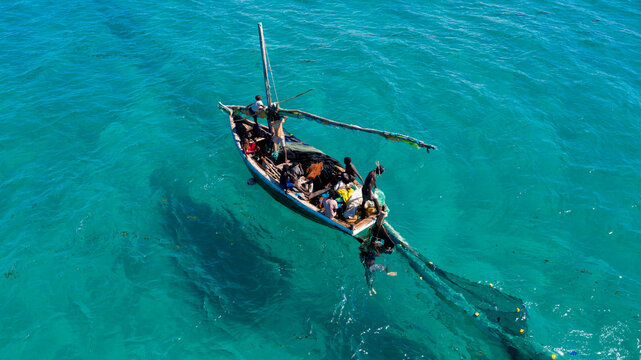 Aerial view of a traditional dhow sails across the turquoise waters of the Indian Ocean, its dark hull a stark contrast against the vibrant sea, Ilha de Mocambique, Nampula, Mozambique.