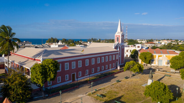 Aerial view of vibrant red buildings contrast with the turquoise sea and clear blue sky, showcasing the unique architecture of the island, Ilha de Mocambique, Nampula, Mozambique.
