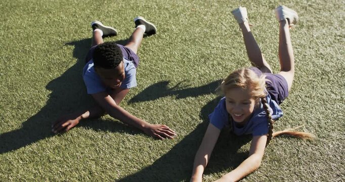 Two school children after playful cue reaching, touching, smiling on sunlit turf with long shadows