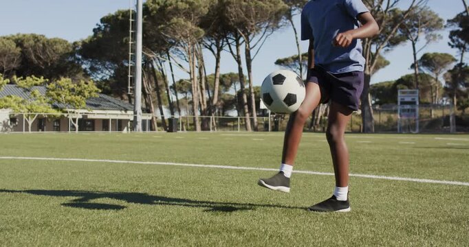 African youth blue shirt practicing with ball at feet tapping juggling dribbling across grass pitch