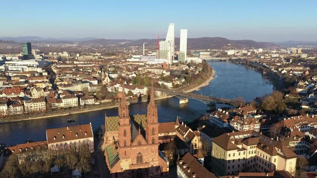 Basel, Switzerland: Cinematic aerial drone footage of Basel old town with the gothic cathedral, the Munster, along the Rhine river on a sunny winter day with modern office towers in Switzerland