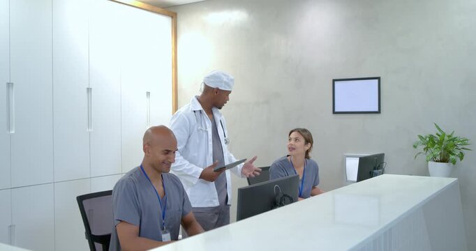 Doctor in coat approaching desk consulting tablet confirming info as staff answering phone  and  typ