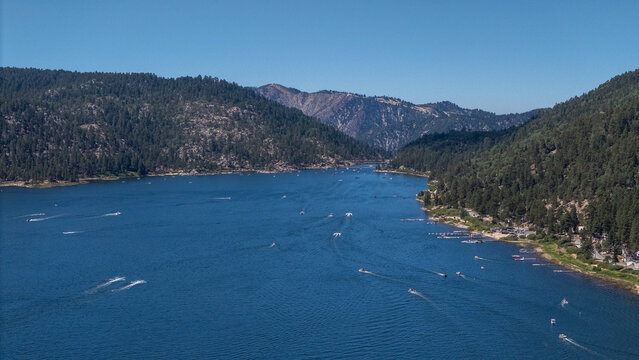 Aerial view of the tranquil big bear lake surrounded by forests, boats cutting through the water, creating a vibrant contrast against the deep blue surface, Lake Arrowhead, California, United States.