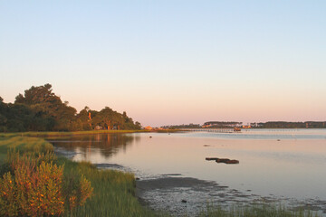 A peaceful Chesapeake Bay morning with warm sunrise light reflecting across calm water, marsh grasses, and distant shoreline trees. Ideal for themes of nature, wetlands, coastal scenery, tranquility,  © Ryan
