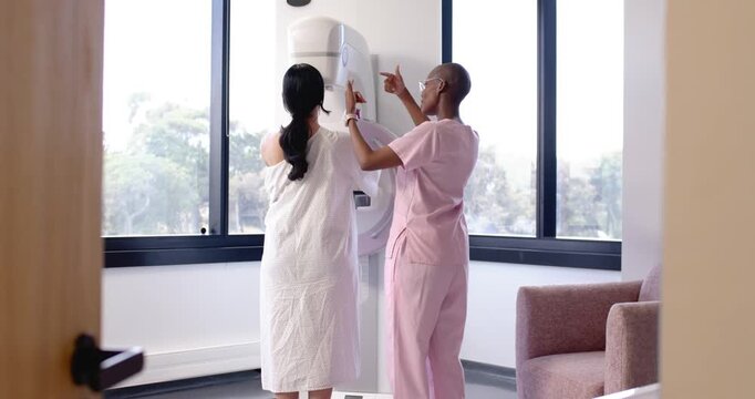 Women African American patient and Hispanic tech positioning at mammogram machine, gown pink scrubs