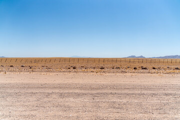 On the way to Swakopmund, an endless road stretches through the striking landscape of the Namib Desert. Vast open plains, arid terrain, and gentle sand dunes meet a wide, dramatic sky.