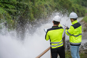 A engineering doing his checking routine. He is wearing hard hat and engineer uniform.Standing by the rail by the dam.Monitor water levels from the heavy rain that has been falling for several days.