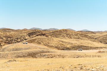 On the way to Swakopmund, an endless road stretches through the striking landscape of the Namib Desert. Vast open plains, arid terrain, and gentle sand dunes meet a wide, dramatic sky.
