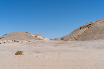 Fototapeta premium On the way to Swakopmund, an endless road stretches through the striking landscape of the Namib Desert. Vast open plains, arid terrain, and gentle sand dunes meet a wide, dramatic sky.