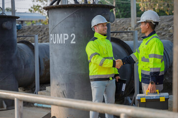 Professional Asian engineers inspecting industrial water pump machinery. Two technicians checking maintenance records on a clipboard at an outdoor construction site factory facility.