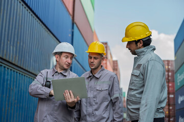 Team of professional logistic engineers inspecting shipping containers at a busy cargo port. Men pointing and discussing global export business plans using a digital tablet technology.