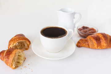 Morning breakfast set with black coffee, milk jug, sweet jam and fresh croissants on bright table. 