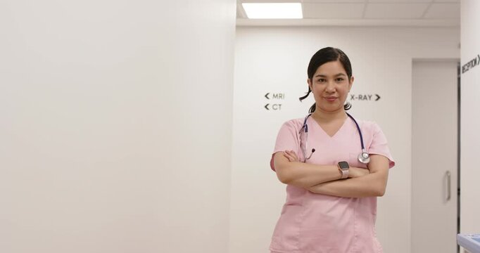 Hispanic woman in pink scrubs standing near MRI sign, arms crossed, smiling after camera move