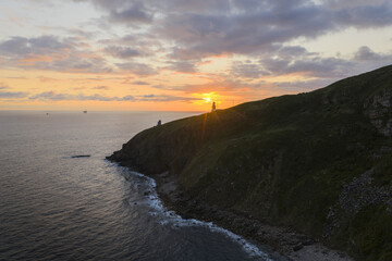 Aerial view of a dramatic coastline where the rugged cliffs meet the ocean under a colorful sky, Gaztelugatxeko Doniene, Basque Country, Spain.