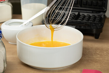 Hand Using a Whisk to Mix Raw Eggs in a White Bowl for Baking Waffles