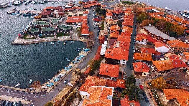 Multiple red-roofed buildings in the cityscape at the waterscape. View on the boats standing on the quay. Seagulls fly over the scenery.