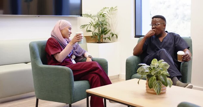 Diverse staff taking break in lounge with coffee one gesturing with stethoscope other eating apple