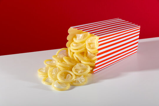 Red popcorn box spilling condoms on a white surface