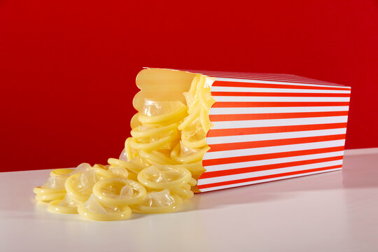Condoms spilling from striped popcorn box on red background