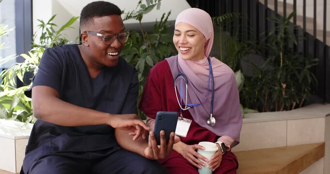 Diverse coworkers left male showing phone, right female smiling with stethoscope in atrium on break