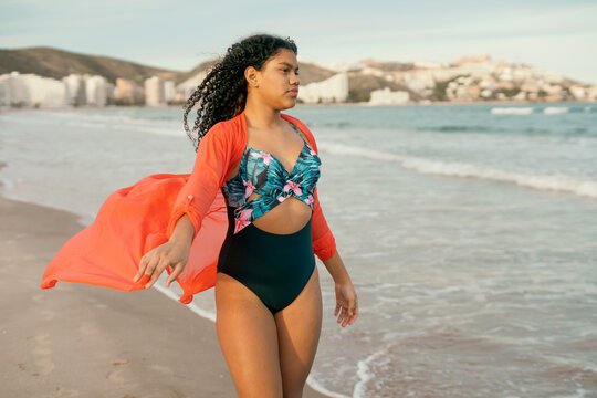 Carefree tourist walking on the seashore with orange pareo waving in the wind,