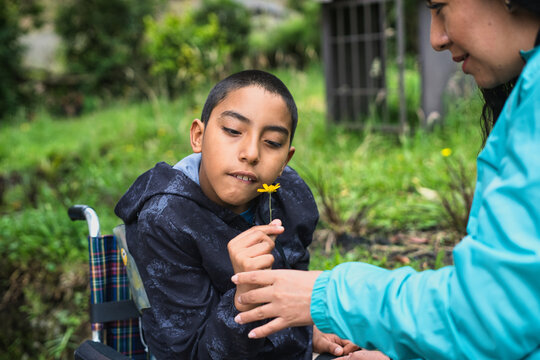 Disabled child smelling a flower with his mother in a park