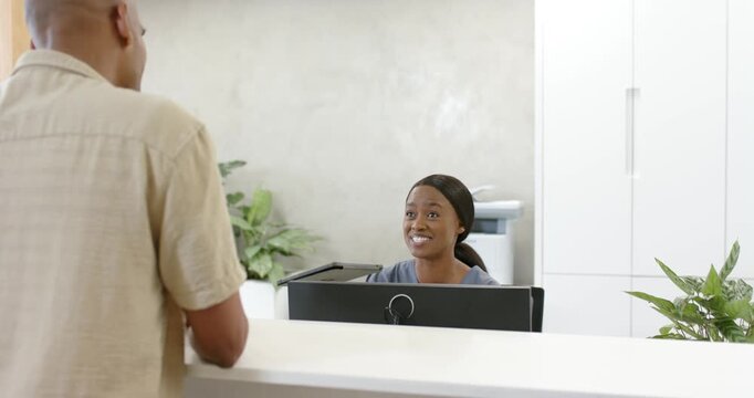 African American receptionist greeting visitor approaching left while checking tablet for ID check