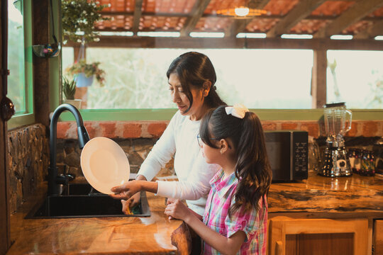 Mother and daughter washing dishes in rustic kitchen
