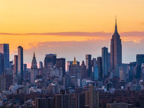 Aerial view of the Empire State Building rising majestically amidst a sprawling cityscape under a warm sky, New York, New York, United States.