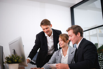 Professional business team collaborating at a desk while reviewing information on a computer in an office setting.