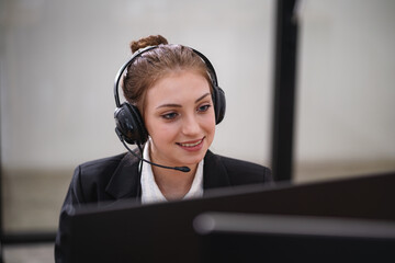Smiling customer support representative wearing a headset while working on a computer in a modern office environment.