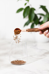 A woman's hand pours instant coffee into a glass with a spoon