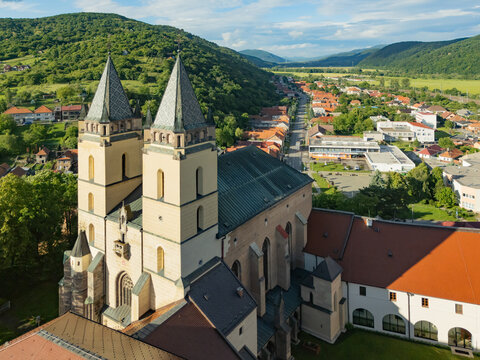 Aerial view of the striking Hronsky Benadik monastery standing proudly against a backdrop of rolling green hills and the distant town, Hronsky Benadik, Banska Bystrica Region, Slovakia.