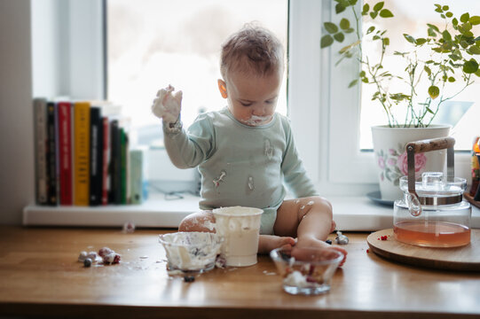 Messy toddler boy sitting on kitchen counter at home, eating.