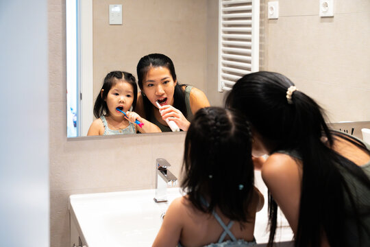 Mother and daughter brushing teeth together in bathroom