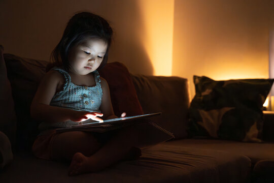 Child using tablet on cozy couch in dim lighting