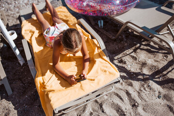 Gril relaxing on beach lounger with smartphone in hand.