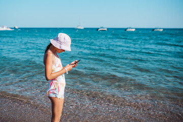 Gril relaxing on beach with smartphone in hand.