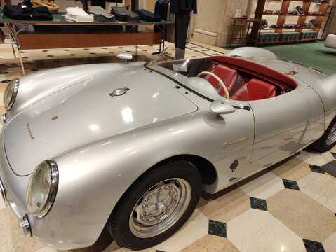 Rome, Italy - January 12, 2026: Classic silver Porsche 550 Spyder sports car displayed in luxury showroom with elegant interior and clothing racks in the background