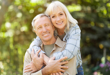 Fototapeta premium Romantic elderly spouses enjoying time together, embracing, sitting in garden at sunny day, spending time outdoors and smiling at camera, copy space
