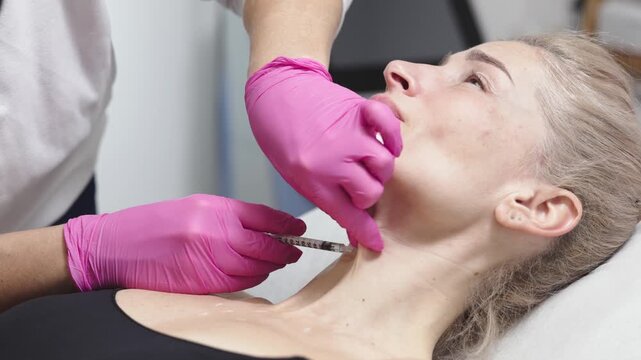 Female patient receiving cosmetic treatment in a beauty clinic, as a practitioner injects dermal filler into her chin area, showcasing the procedure's progression and technique