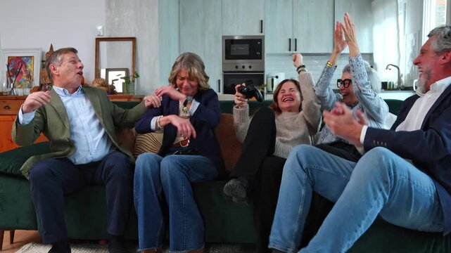Excited senior friends playing video games together at home