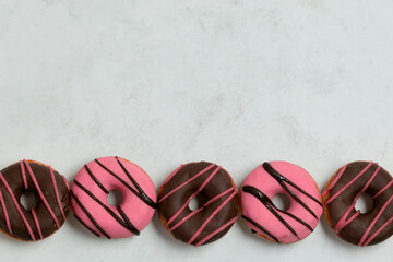 Pink and Chocolate Donuts in a Row on Light Background