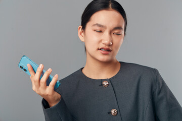 Young woman holding smartphone with disgusted facial expression in studio. Portrait of female person showing dislike or frustration with mobile device on gray background.