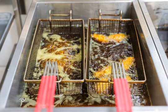 close up of two Baskets Frying Food in Hot Oil on fast food restaurant kitchen